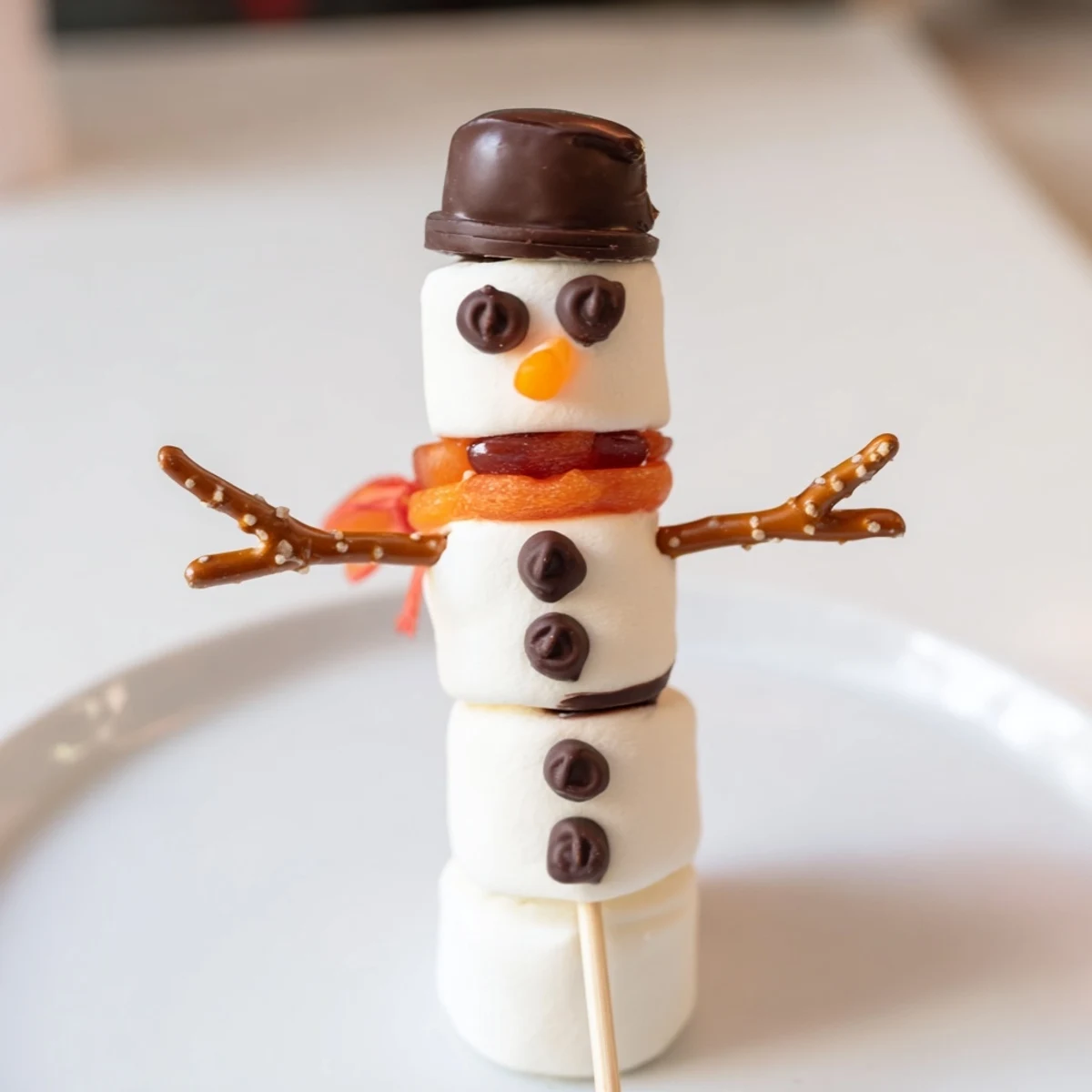 These cute Marshmallow Snowman Sticks feature cheerful faces and colorful scarves, perfect for a kids' snack.