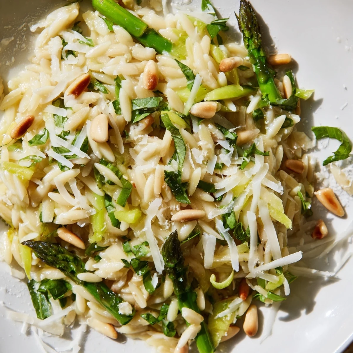 Golden-brown orzo pasta topped with bright green shaved asparagus ribbons, toasted pine nuts, and a zesty lemon-olive oil dressing, ready to serve.  