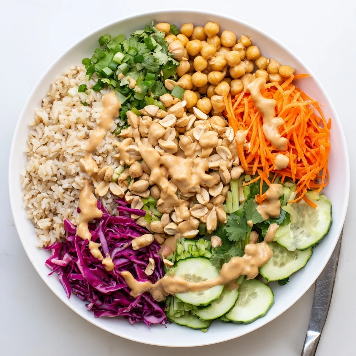 A close-up of a vibrant Peanut Chickpea Rice Bowl topped with shredded carrots, red cabbage, and roasted peanuts.