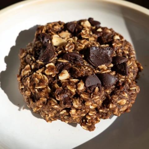 Shiny, dark chocolate oatmeal breakfast cookies piled on a baking sheet, ready to cool.