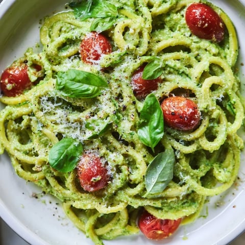 Fresh avocado pesto coats spiralized zucchini noodles, topped with halved cherry tomatoes and basil for a vibrant, low-carb main dish.  