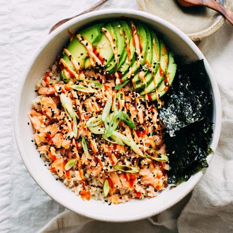 Golden microwaved rice with tender salmon flakes, bright green avocado slices, and sesame seeds garnish this Emily Mariko Salmon Rice Bowl, served with crispy seaweed.