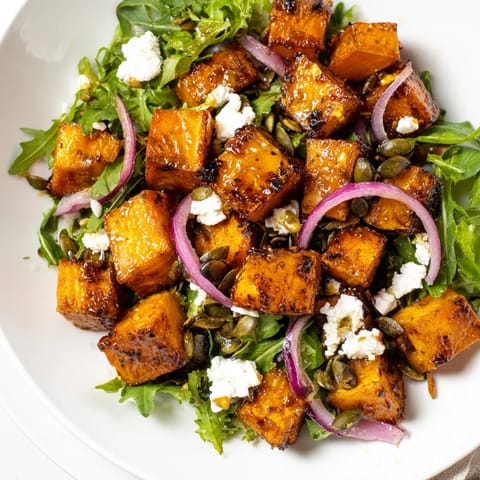 Golden roasted sweet potato salad in a white bowl, featuring peppery arugula, red onion slices, and a drizzle of tangy honey-lime dressing.