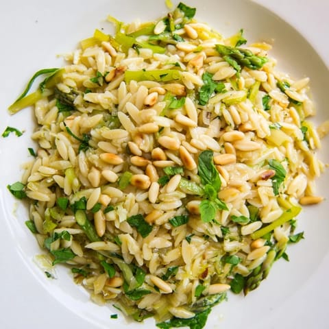 Fresh Asparagus Lemon Orzo Salad with shaved greens, grated Parmesan, and lemon vinaigrette, garnished with basil and parsley for a spring meal.  