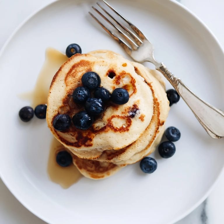 A close-up of tender cottage cheese pancakes topped with sliced bananas and a dusting of powdered sugar.