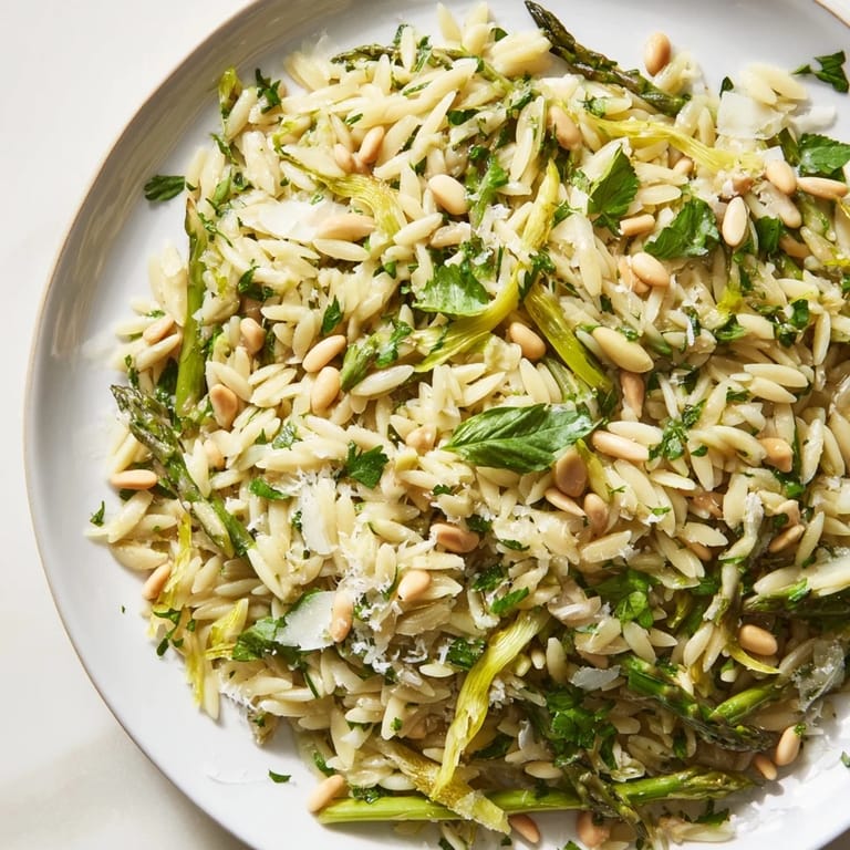 A vibrant bowl of spring Asparagus Lemon Orzo Salad, featuring shaved asparagus and pine nuts tossed in a zesty lemon dressing.
