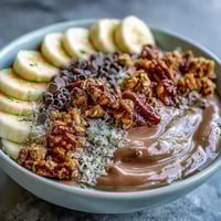 Chunky Monkey Smoothie Bowls topped with crunchy granola and sliced bananas in a white bowl.