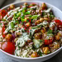 A close-up of New Years Hoppin John Salad with black-eyed peas, chickpeas, and vibrant red bell peppers in a creamy tahini dressing.