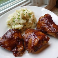 Golden-glazed honey BBQ chicken thighs, presented with a side of fluffy garlic mashed potatoes.